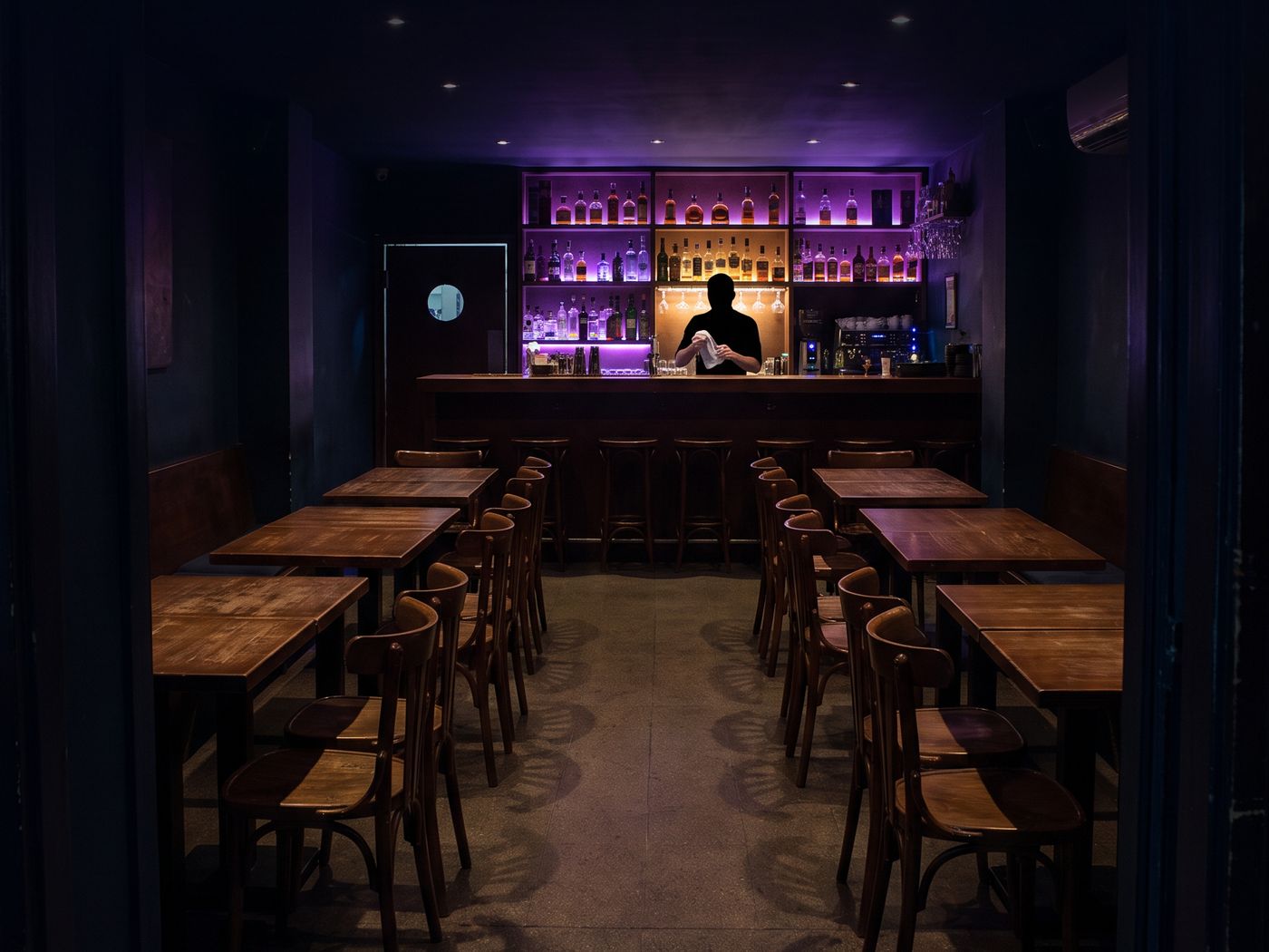 A bar at eleven at night with every chair empty and one bartender behind the counter